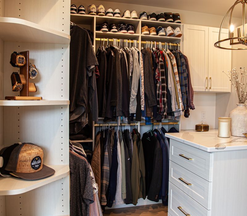 White cabinetry and shelving, a wood floor, and a gold chandelier add beauty to this functional walk-in closet that includes a washer and dryer.