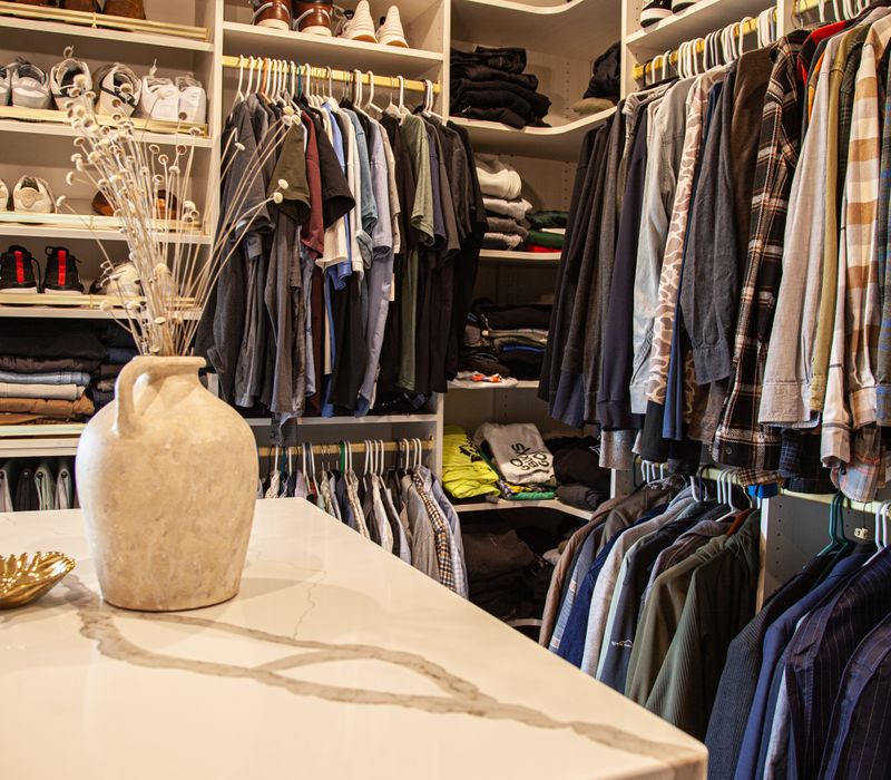 White cabinetry and shelving, a wood floor, and a gold chandelier add beauty to this functional walk-in closet that includes a washer and dryer.