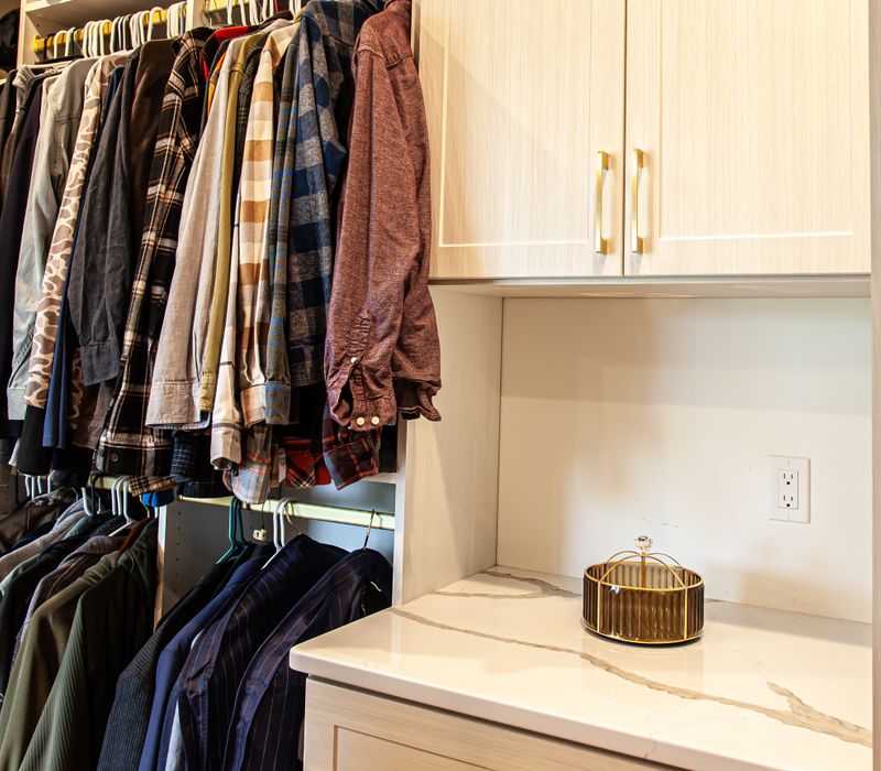 White cabinetry and shelving, a wood floor, and a gold chandelier add beauty to this functional walk-in closet that includes a washer and dryer.