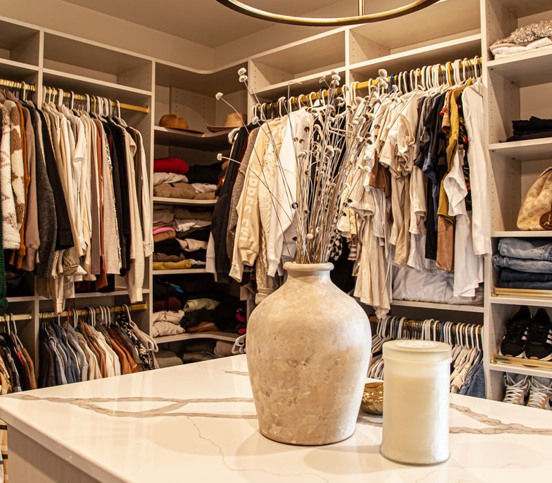 White cabinetry and shelving, a wood floor, and a gold chandelier add beauty to this functional walk-in closet that includes a washer and dryer.