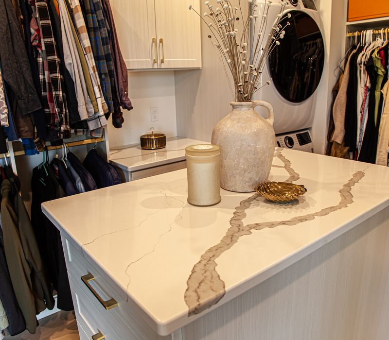 White cabinetry and shelving, a wood floor, and a gold chandelier add beauty to this functional walk-in closet that includes a washer and dryer.