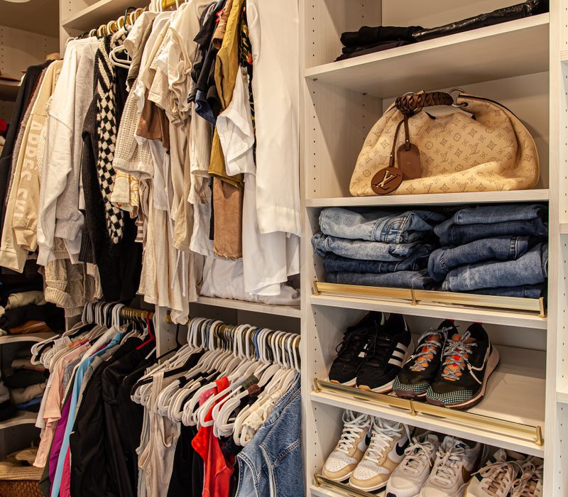 White cabinetry and shelving, a wood floor, and a gold chandelier add beauty to this functional walk-in closet that includes a washer and dryer.