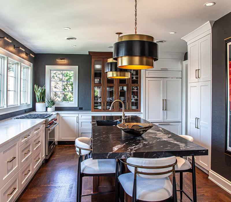 This complete kitchen remodel utilizes timeless materials, an intelligent reconfiguration of the space, and an effortless blend of natural light and warmth. It features cabinetry by DHDK, black quartzite countertops, herringbone wood flooring, a Broan pop-up downdraft hood, and a wet bar.