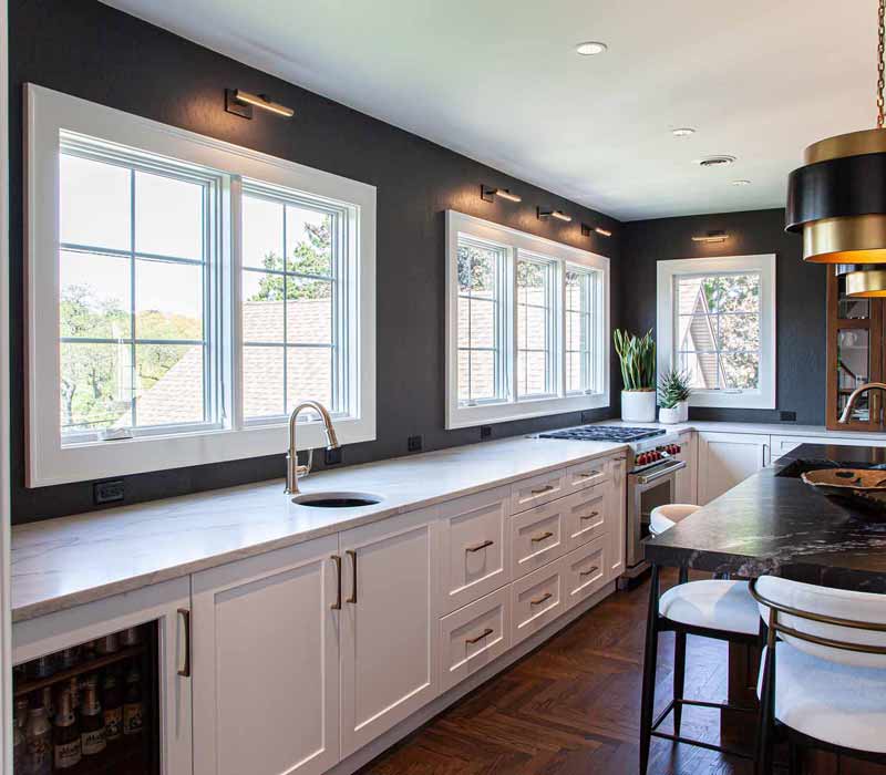 This complete kitchen remodel utilizes timeless materials, an intelligent reconfiguration of the space, and an effortless blend of natural light and warmth. It features cabinetry by DHDK, black quartzite countertops, herringbone wood flooring, a Broan pop-up downdraft hood, and a wet bar.