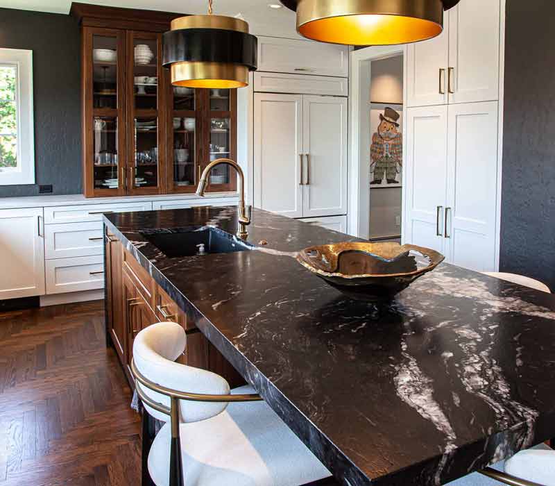 This complete kitchen remodel utilizes timeless materials, an intelligent reconfiguration of the space, and an effortless blend of natural light and warmth. It features cabinetry by DHDK, black quartzite countertops, herringbone wood flooring, a Broan pop-up downdraft hood, and a wet bar.