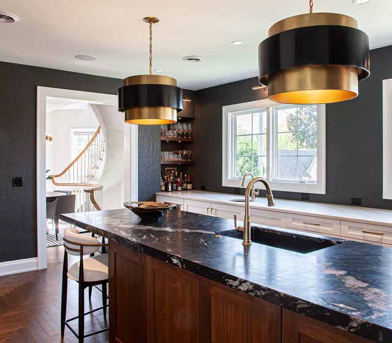 This complete kitchen remodel utilizes timeless materials, an intelligent reconfiguration of the space, and an effortless blend of natural light and warmth. It features cabinetry by DHDK, black quartzite countertops, herringbone wood flooring, a Broan pop-up downdraft hood, and a wet bar.