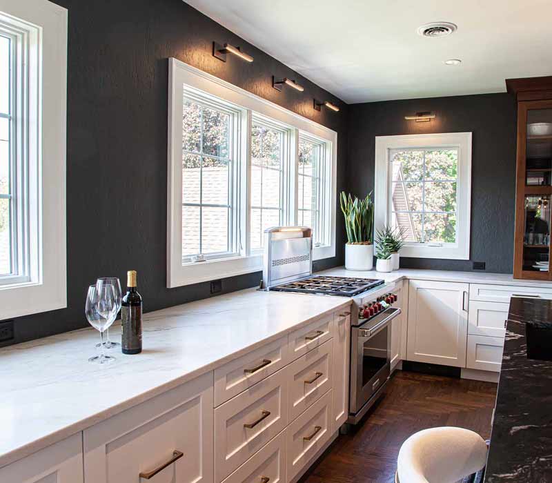 This complete kitchen remodel utilizes timeless materials, an intelligent reconfiguration of the space, and an effortless blend of natural light and warmth. It features cabinetry by DHDK, black quartzite countertops, herringbone wood flooring, a Broan pop-up downdraft hood, and a wet bar.