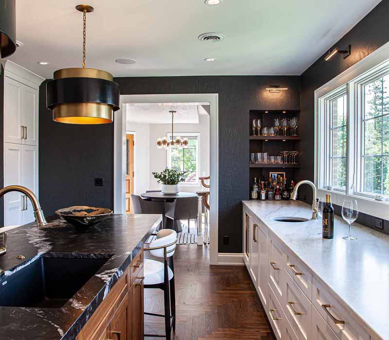 This complete kitchen remodel utilizes timeless materials, an intelligent reconfiguration of the space, and an effortless blend of natural light and warmth. It features cabinetry by DHDK, black quartzite countertops, herringbone wood flooring, a Broan pop-up downdraft hood, and a wet bar.