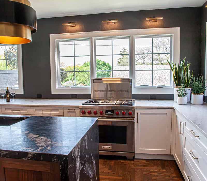 This complete kitchen remodel utilizes timeless materials, an intelligent reconfiguration of the space, and an effortless blend of natural light and warmth. It features cabinetry by DHDK, black quartzite countertops, herringbone wood flooring, a Broan pop-up downdraft hood, and a wet bar.