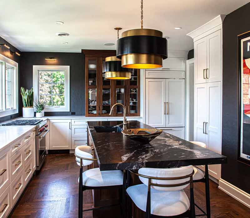 This complete kitchen remodel utilizes timeless materials, an intelligent reconfiguration of the space, and an effortless blend of natural light and warmth. It features cabinetry by DHDK, black quartzite countertops, herringbone wood flooring, a Broan pop-up downdraft hood, and a wet bar.