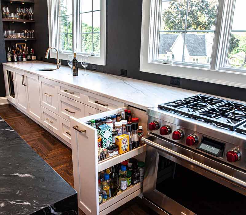 This complete kitchen remodel utilizes timeless materials, an intelligent reconfiguration of the space, and an effortless blend of natural light and warmth. It features cabinetry by DHDK, black quartzite countertops, herringbone wood flooring, a Broan pop-up downdraft hood, and a wet bar.