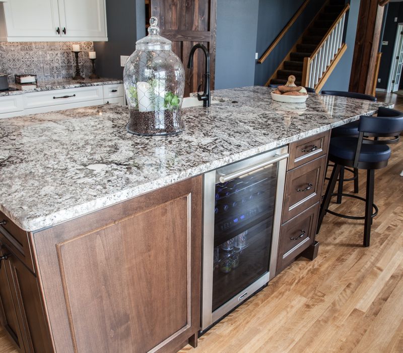 This kitchen combines patterned wall tile, stone countertops, Edison pendant lights, and elegant white cabinetry with a rustic barn door pantry and heavy wooden beams to define the space.