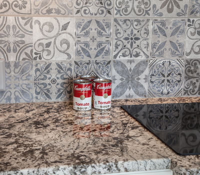This kitchen combines patterned wall tile, stone countertops, Edison pendant lights, and elegant white cabinetry with a rustic barn door pantry and heavy wooden beams to define the space.