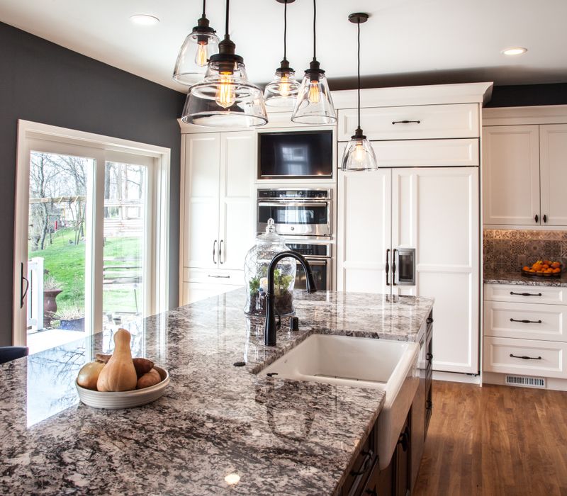 This kitchen combines patterned wall tile, stone countertops, Edison pendant lights, and elegant white cabinetry with a rustic barn door pantry and heavy wooden beams to define the space.