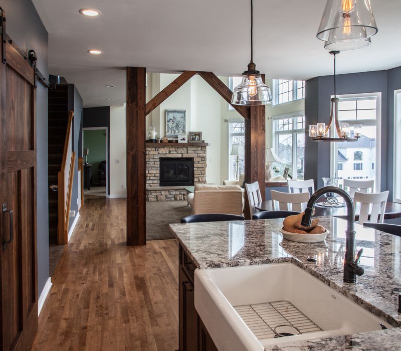 This kitchen combines patterned wall tile, stone countertops, Edison pendant lights, and elegant white cabinetry with a rustic barn door pantry and heavy wooden beams to define the space.