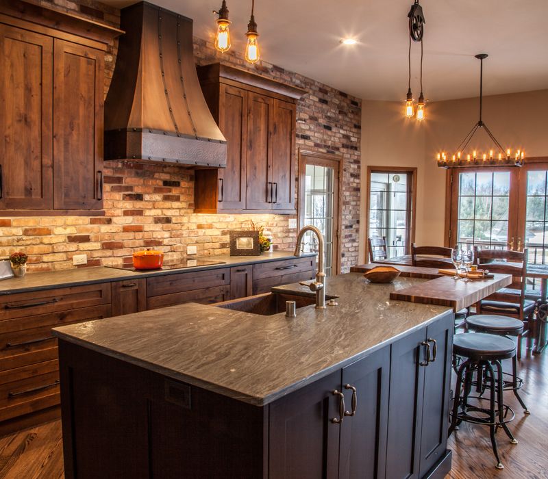 Rustic brick walls, rough-hewn beams, an end-grain cutting board, and a hammered copper sink and range hood add texture to this woodsy open concept kitchen.