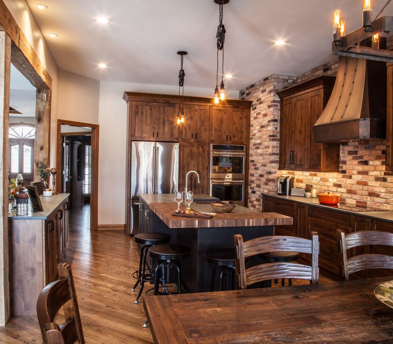 Rustic brick walls, rough-hewn beams, an end-grain cutting board, and a hammered copper sink and range hood add texture to this woodsy open concept kitchen.