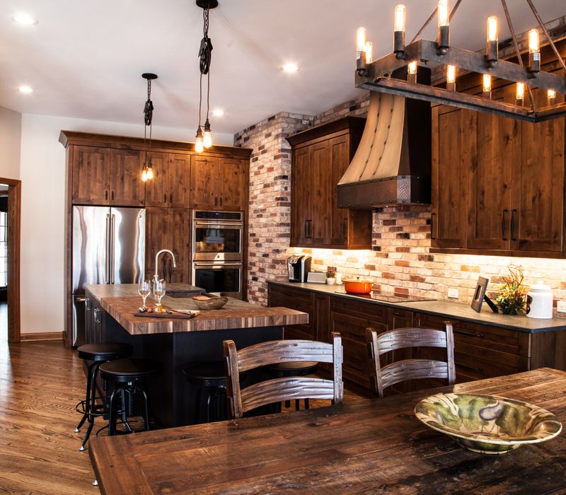 Rustic brick walls, rough-hewn beams, an end-grain cutting board, and a hammered copper sink and range hood add texture to this woodsy open concept kitchen.