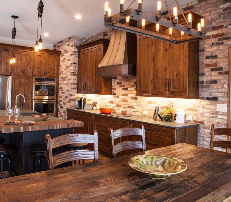 Rustic brick walls, rough-hewn beams, an end-grain cutting board, and a hammered copper sink and range hood add texture to this woodsy open concept kitchen.