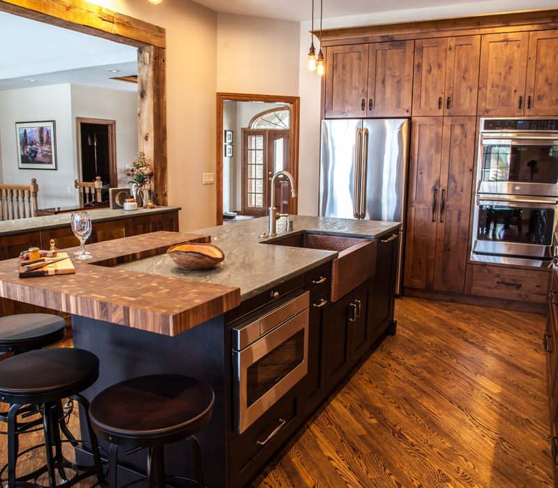 Rustic brick walls, rough-hewn beams, an end-grain cutting board, and a hammered copper sink and range hood add texture to this woodsy open concept kitchen.