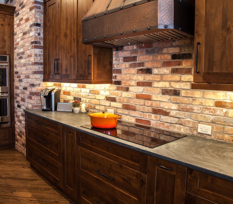 Rustic brick walls, rough-hewn beams, an end-grain cutting board, and a hammered copper sink and range hood add texture to this woodsy open concept kitchen.
