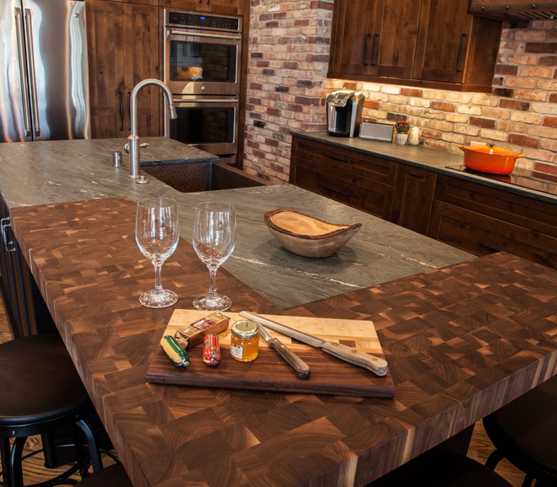 Rustic brick walls, rough-hewn beams, an end-grain cutting board, and a hammered copper sink and range hood add texture to this woodsy open concept kitchen.