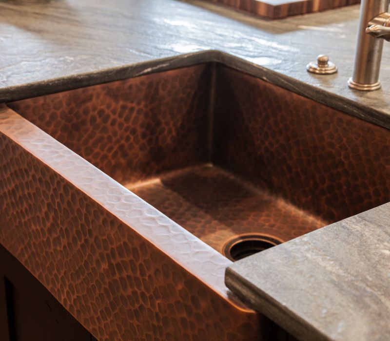 Rustic brick walls, rough-hewn beams, an end-grain cutting board, and a hammered copper sink and range hood add texture to this woodsy open concept kitchen.