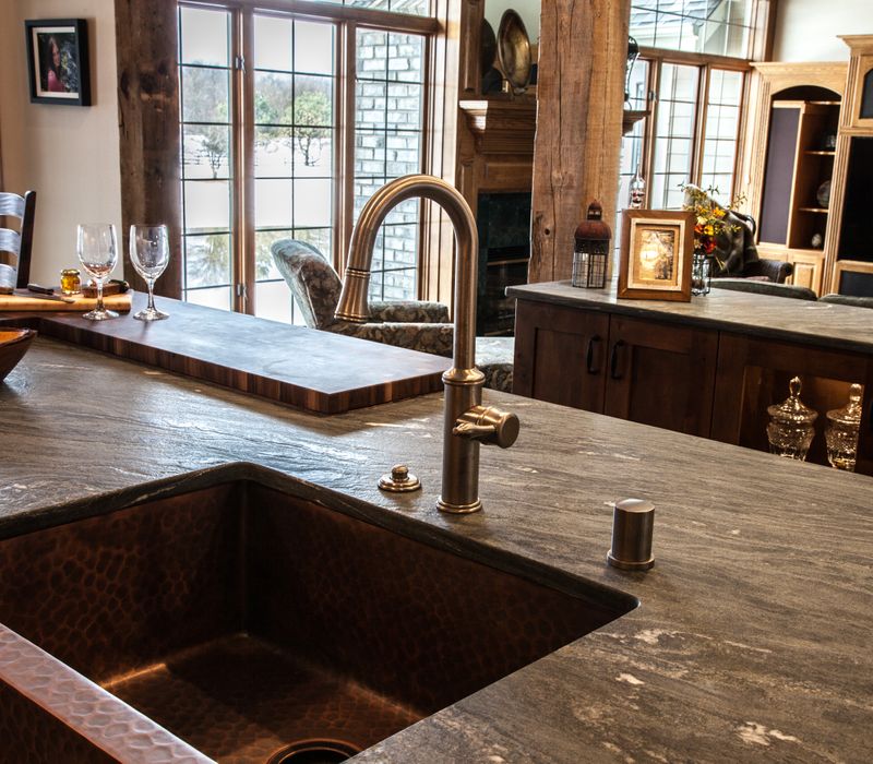 Rustic brick walls, rough-hewn beams, an end-grain cutting board, and a hammered copper sink and range hood add texture to this woodsy open concept kitchen.