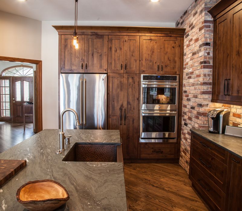 Rustic brick walls, rough-hewn beams, an end-grain cutting board, and a hammered copper sink and range hood add texture to this woodsy open concept kitchen.