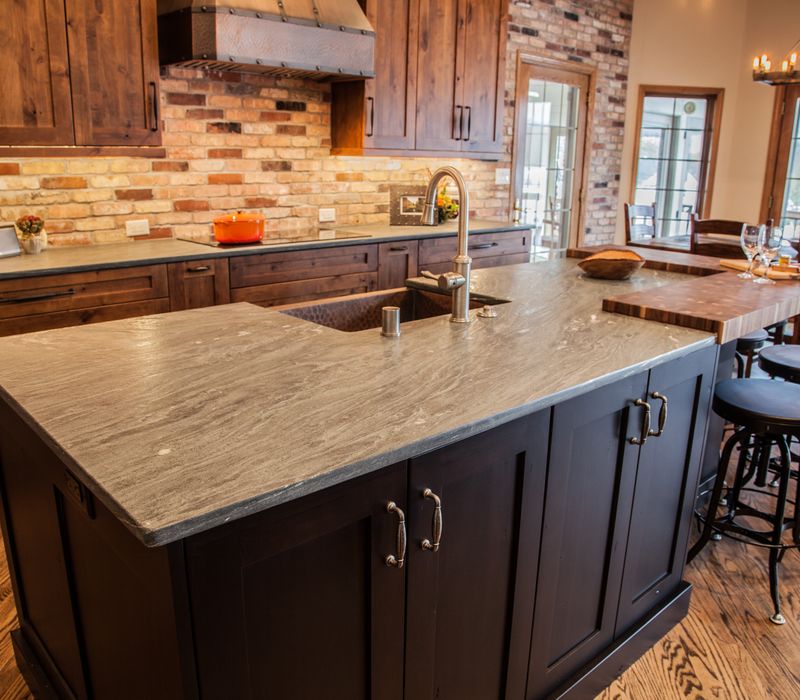 Rustic brick walls, rough-hewn beams, an end-grain cutting board, and a hammered copper sink and range hood add texture to this woodsy open concept kitchen.