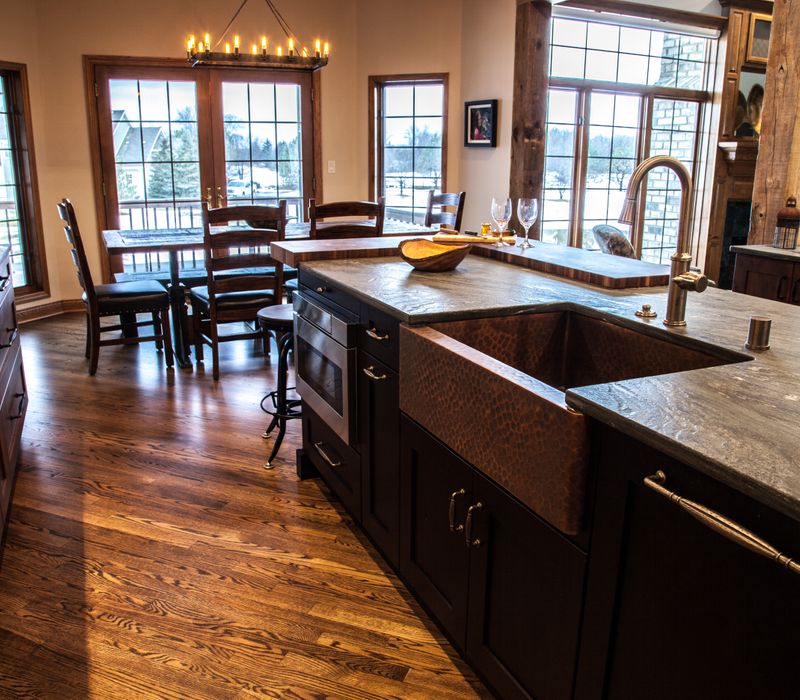 Rustic brick walls, rough-hewn beams, an end-grain cutting board, and a hammered copper sink and range hood add texture to this woodsy open concept kitchen.
