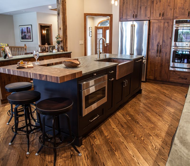 Rustic brick walls, rough-hewn beams, an end-grain cutting board, and a hammered copper sink and range hood add texture to this woodsy open concept kitchen.