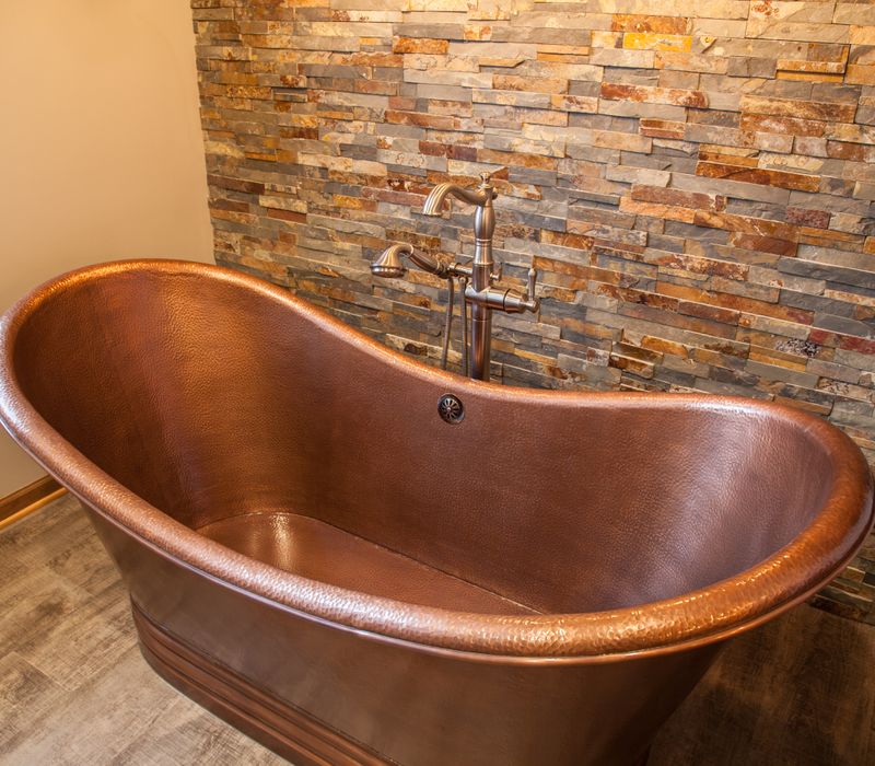 Rustic brick walls, rough-hewn beams, an end-grain cutting board, and a hammered copper sink and range hood add texture to this woodsy open concept kitchen.