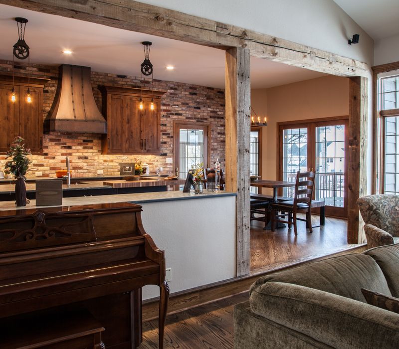 Rustic brick walls, rough-hewn beams, an end-grain cutting board, and a hammered copper sink and range hood add texture to this woodsy open concept kitchen.