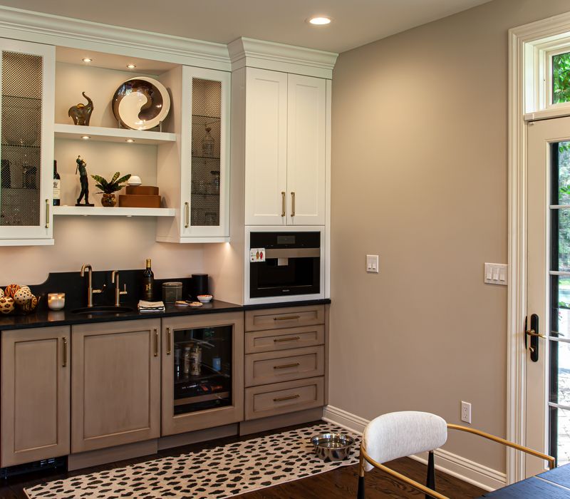 This warm, inviting kitchen features modern brushed gold chandeliers, marble countertops with gold veins, an end-grain cutting board, a metallic glass tile backsplash, and a black range hood with brass accents.