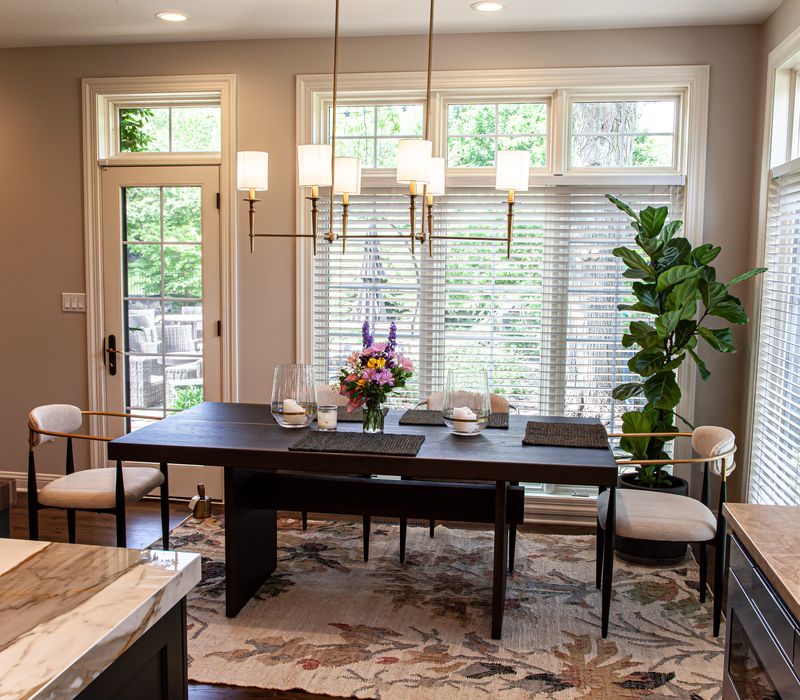 This warm, inviting kitchen features modern brushed gold chandeliers, marble countertops with gold veins, an end-grain cutting board, a metallic glass tile backsplash, and a black range hood with brass accents.