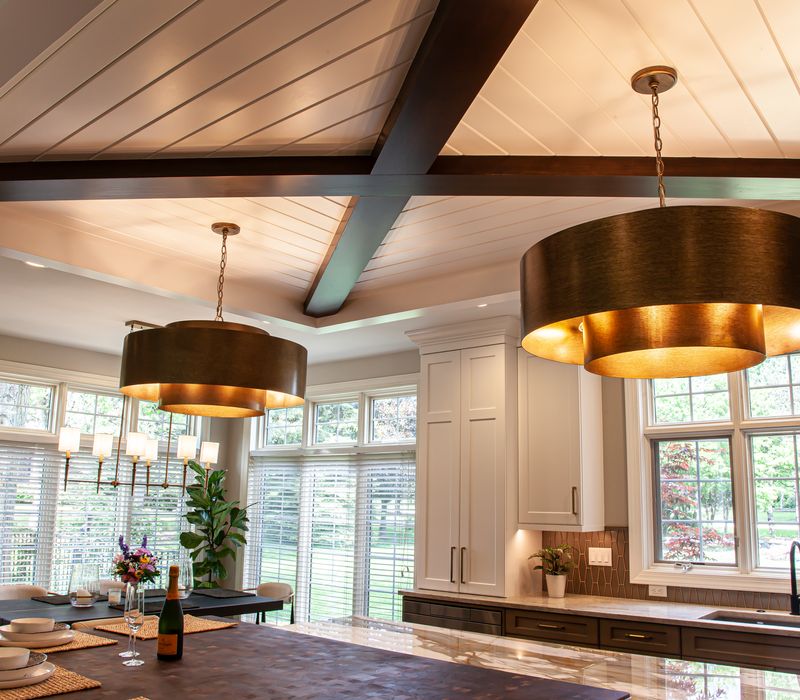 This warm, inviting kitchen features modern brushed gold chandeliers, marble countertops with gold veins, an end-grain cutting board, a metallic glass tile backsplash, and a black range hood with brass accents.