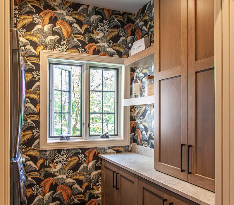 This warm, inviting kitchen features modern brushed gold chandeliers, marble countertops with gold veins, an end-grain cutting board, a metallic glass tile backsplash, and a black range hood with brass accents.