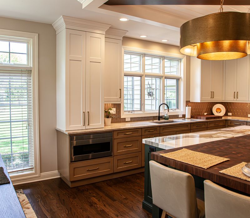This warm, inviting kitchen features modern brushed gold chandeliers, marble countertops with gold veins, an end-grain cutting board, a metallic glass tile backsplash, and a black range hood with brass accents.