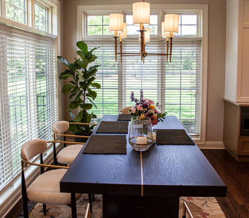 This warm, inviting kitchen features modern brushed gold chandeliers, marble countertops with gold veins, an end-grain cutting board, a metallic glass tile backsplash, and a black range hood with brass accents.