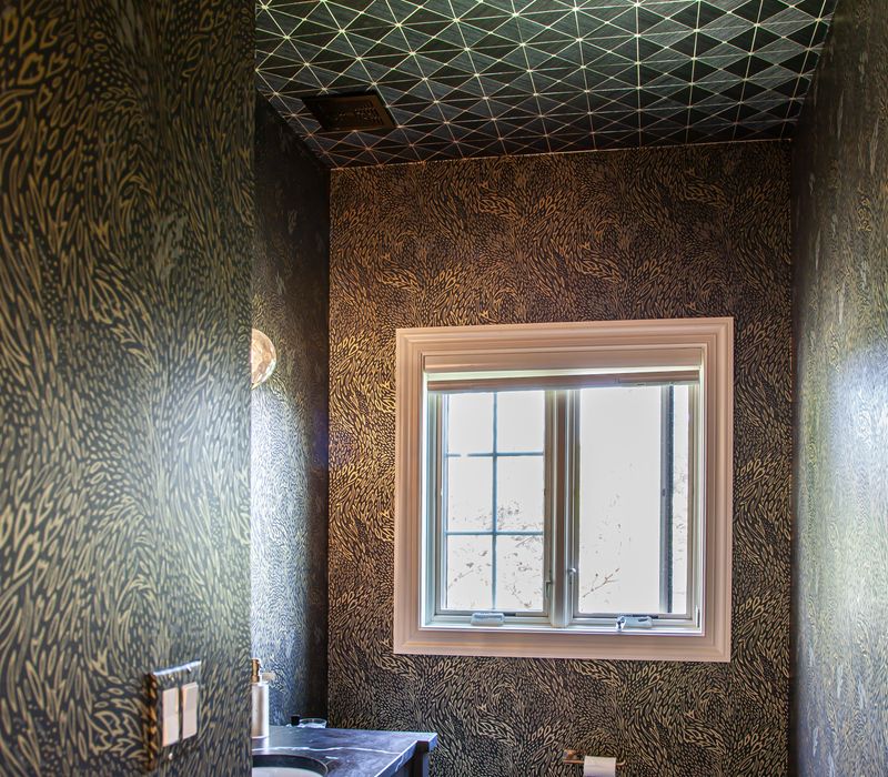 This warm, inviting kitchen features modern brushed gold chandeliers, marble countertops with gold veins, an end-grain cutting board, a metallic glass tile backsplash, and a black range hood with brass accents.