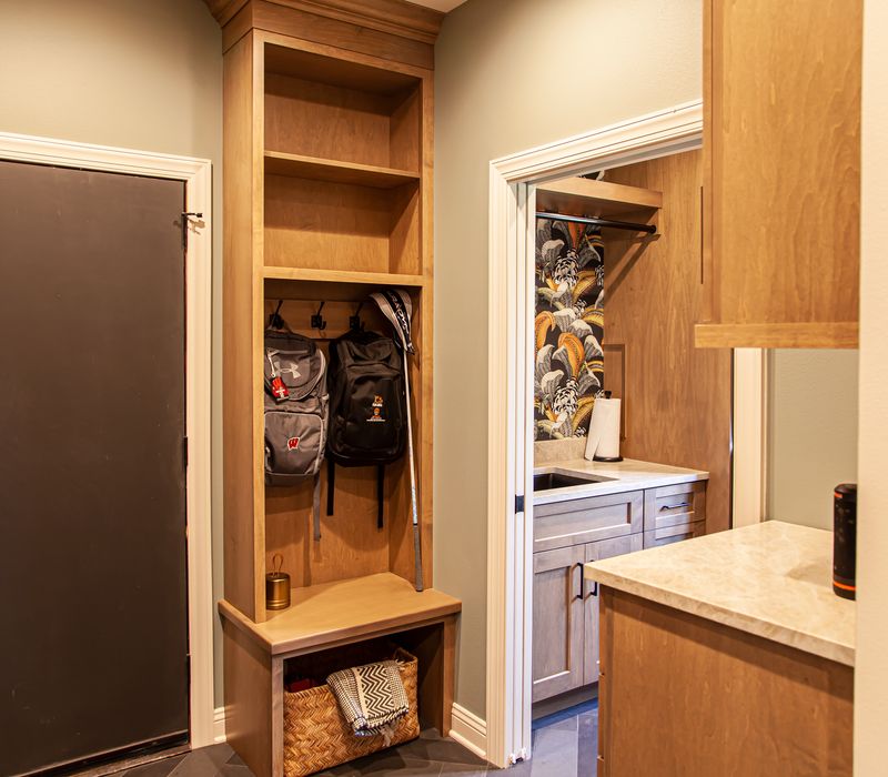 This warm, inviting kitchen features modern brushed gold chandeliers, marble countertops with gold veins, an end-grain cutting board, a metallic glass tile backsplash, and a black range hood with brass accents.