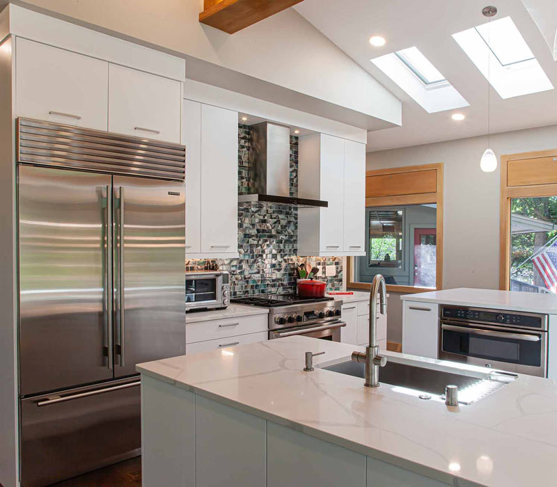 This kitchen remodel celebrates family, nature, and the unique geometry of the original home. It features crisp white cabinetry, cool-toned quartz countertops, two islands, and bold blue accents, plus a tactile mix of materials—wood, metal, glass, and stone—selected to stand the test of time in both durability and style.