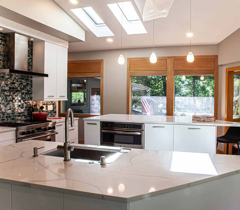 This kitchen remodel celebrates family, nature, and the unique geometry of the original home. It features crisp white cabinetry, cool-toned quartz countertops, two islands, and bold blue accents, plus a tactile mix of materials—wood, metal, glass, and stone—selected to stand the test of time in both durability and style.