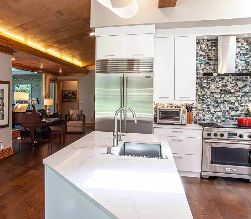 This kitchen remodel celebrates family, nature, and the unique geometry of the original home. It features crisp white cabinetry, cool-toned quartz countertops, two islands, and bold blue accents, plus a tactile mix of materials—wood, metal, glass, and stone—selected to stand the test of time in both durability and style.