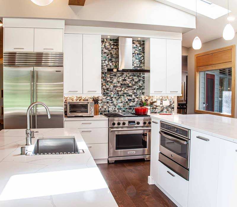 This kitchen remodel celebrates family, nature, and the unique geometry of the original home. It features crisp white cabinetry, cool-toned quartz countertops, two islands, and bold blue accents, plus a tactile mix of materials—wood, metal, glass, and stone—selected to stand the test of time in both durability and style.