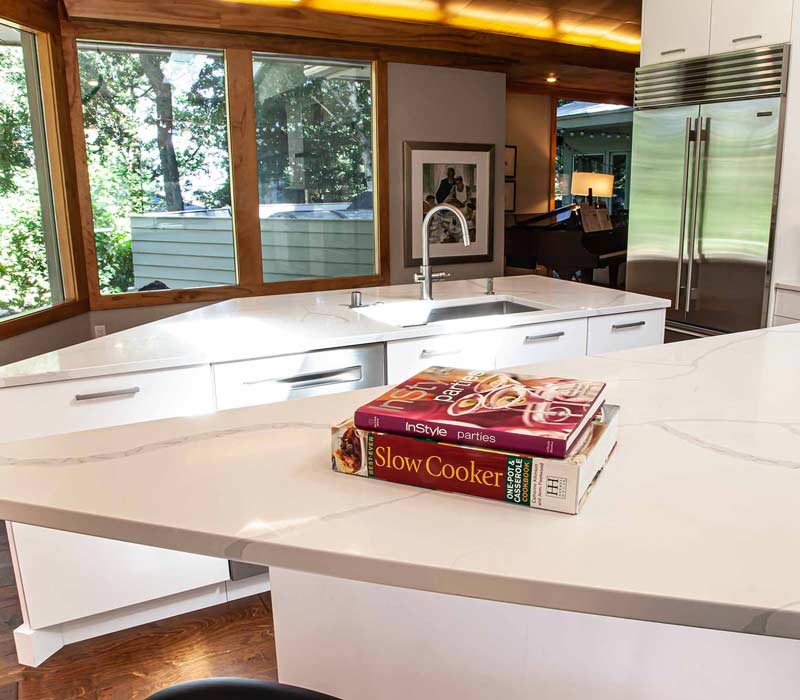 This kitchen remodel celebrates family, nature, and the unique geometry of the original home. It features crisp white cabinetry, cool-toned quartz countertops, two islands, and bold blue accents, plus a tactile mix of materials—wood, metal, glass, and stone—selected to stand the test of time in both durability and style.