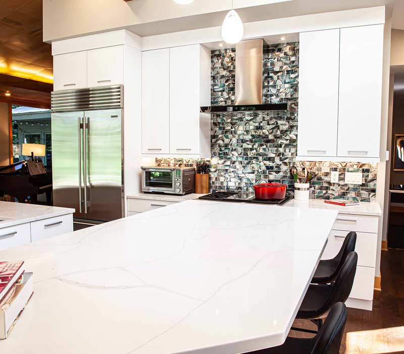 This kitchen remodel celebrates family, nature, and the unique geometry of the original home. It features crisp white cabinetry, cool-toned quartz countertops, two islands, and bold blue accents, plus a tactile mix of materials—wood, metal, glass, and stone—selected to stand the test of time in both durability and style.