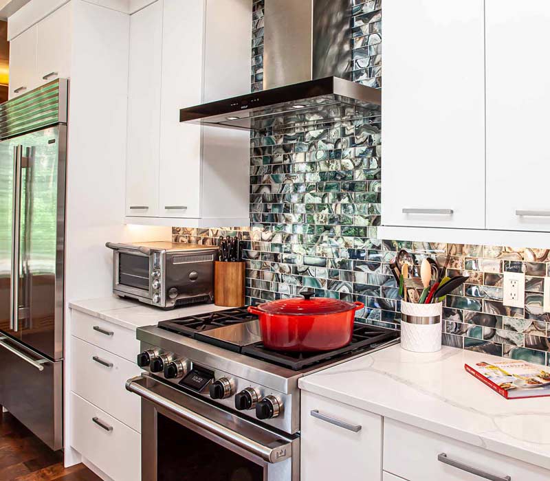 This kitchen remodel celebrates family, nature, and the unique geometry of the original home. It features crisp white cabinetry, cool-toned quartz countertops, two islands, and bold blue accents, plus a tactile mix of materials—wood, metal, glass, and stone—selected to stand the test of time in both durability and style.