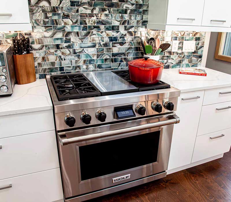 This kitchen remodel celebrates family, nature, and the unique geometry of the original home. It features crisp white cabinetry, cool-toned quartz countertops, two islands, and bold blue accents, plus a tactile mix of materials—wood, metal, glass, and stone—selected to stand the test of time in both durability and style.